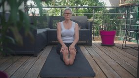 Cinematic storytelling video of a senior old woman practicing yoga and stretching fitness at home. Representation of healthy lifestyle and leisure activities during seniority and the third age