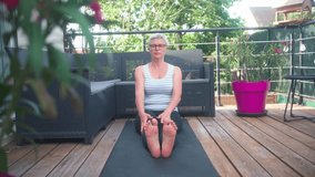 Cinematic storytelling video of a mature woman practicing yoga and stretching fitness at terrace. Representation of healthy lifestyle and leisure activities during middle age