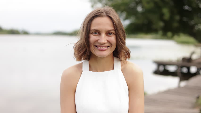 Portrait of stylish young attractive natural beauty caucasian woman with short healthy hair smiling outdoor at nature by the pond on summer. Elegant romantic model girl without makeup looks at camera. Royalty-Free Stock Footage #1107309897