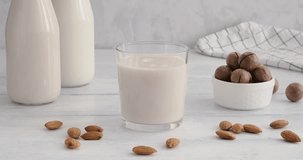 Almond milk. close-up video of womans hand taking a glass with vegan milk made of almonds, grabbing a glass from white table, alternative non-dairy drink, 4k video, slow motion footage