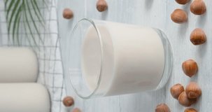 Hazelnut milk, person grabbing a glass of vegan drink made of hazelnuts from table, milk bottles on background, close-up video clip, 4k vertical footage, slow motion video, alternative non-dairy milk