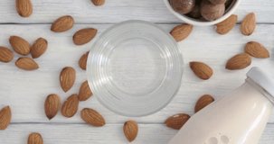 Alternative milk, pouring almond milk into a glass placed on table from bottle, vegan drink made of almond nuts, slow motion video clip, non-dairy product, top table view, horizontal 4k footage