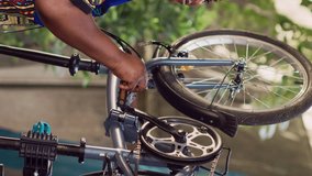 Vertical video African american woman attentively checking bike components ensuring smooth and efficient summer leisure cycling. Smiling female cyclist performing bicycle maintenance. Side-view