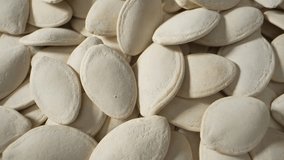 Macro video of pumpkin seeds showcases their intricate textures, featuring a mosaic of earthy hues, fine ridges, and delicate curves. Source of numerous health benefits. 
