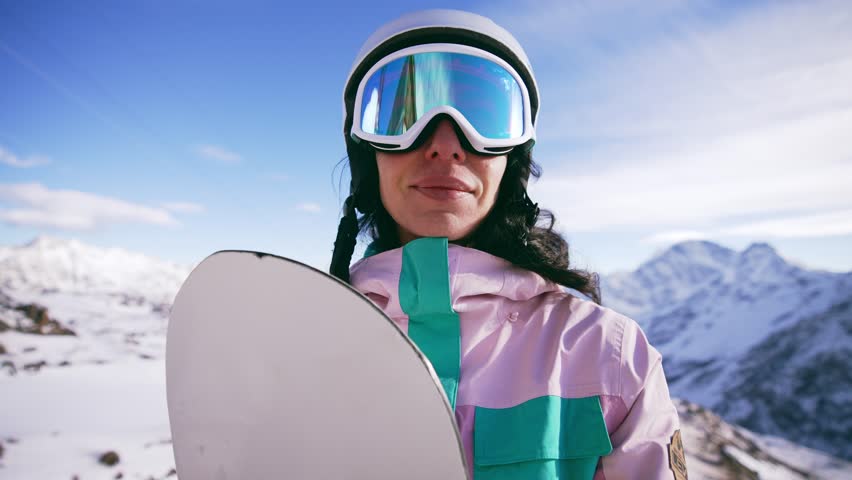 Portrait of happy smiling woman snowboarder in protective helmet and glasses in mountains holding snowboard. Girl wears in ski clothes in winter resort. Enjoy healthy sport active rest, snowboarding. Royalty-Free Stock Footage #1107324499