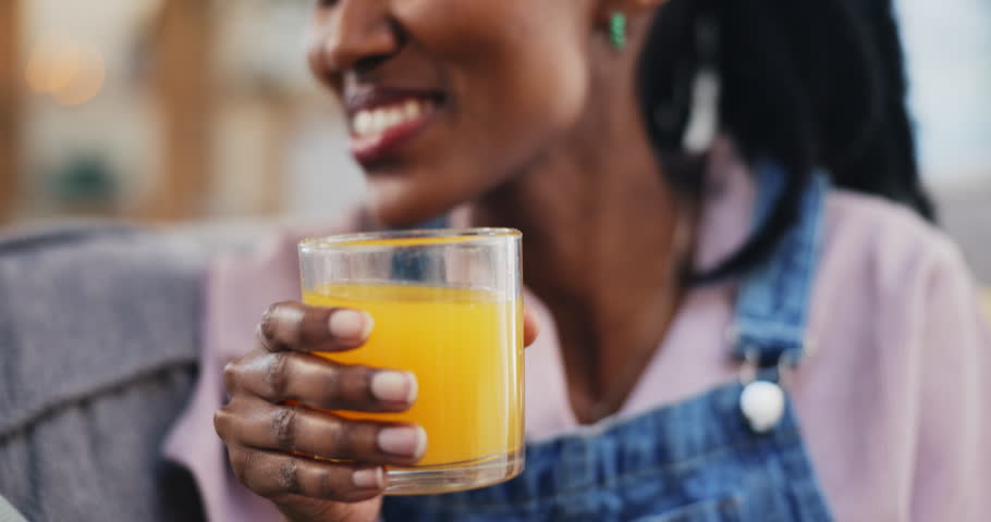 Happy, black woman and orange juice in home living room on sofa in healthy diet, nutrition and wellness. African person, smile and drink fruit glass in hydration, organic vitamin c or vegan benefits