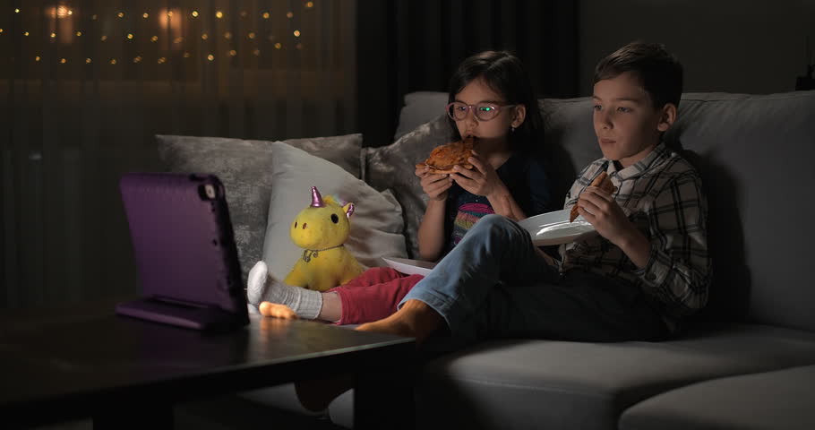 Children watching video on tablet on the sofa at home for entertainment or comedy. Excited kids siblings with tech for streaming a movie with online app in the living room while eating pizza Royalty-Free Stock Footage #1107329375