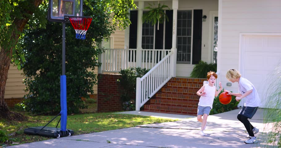 happy kids playing basketball at the driveway of their home. portable basketball hoop stand. active lifestyle. neighborhood activity sports