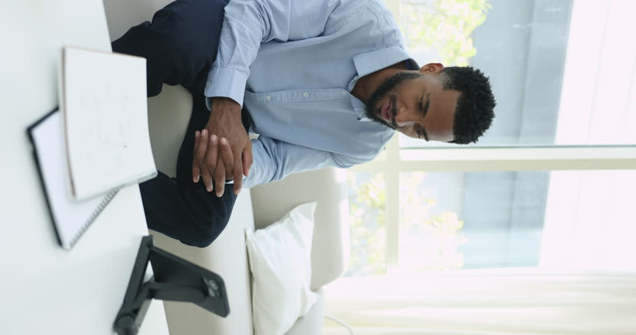 African man makes speech at smart phone camera, takes part in stream, on-line communication, record blog or stories for social media sit on sofa at home, vertical view. Modern tech, videocall event