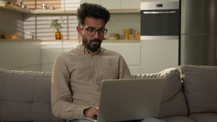 Tired Arabian Indian man freelancer overworked computer laptop work on home couch take off eyeglasses rub dry eyes discomfort eye tension exhausted male guy feel pain due glasses bad eyesight headache Royalty-Free Stock Footage #1107337775