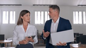 Two diverse partners walking mature Latin business man and European business woman discussing project on gadget in office. Two colleagues of professional business people working together at workspace. - Powered by Shutterstock - Get 15% off with code: PIKWIZARD15