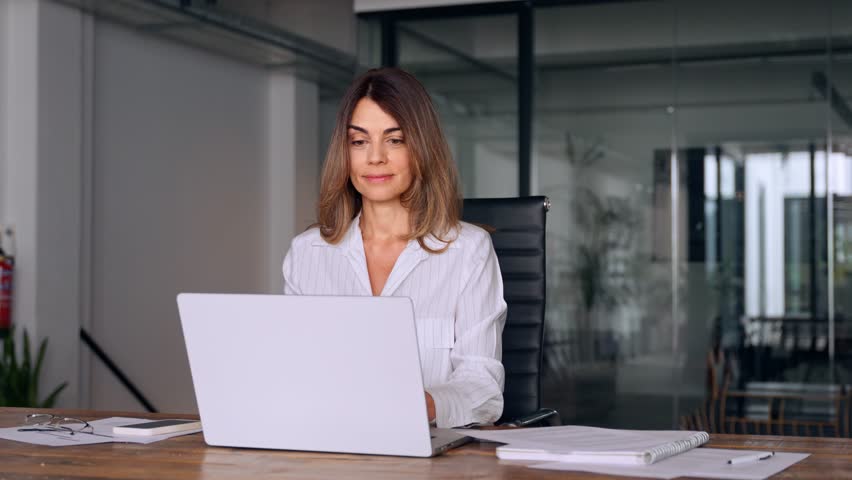 40s mid age European business woman CEO using laptop application for work sitting at table workspace in office. Smiling Latin Hispanic mature adult professional businesswoman using pc digital computer Royalty-Free Stock Footage #1107342067