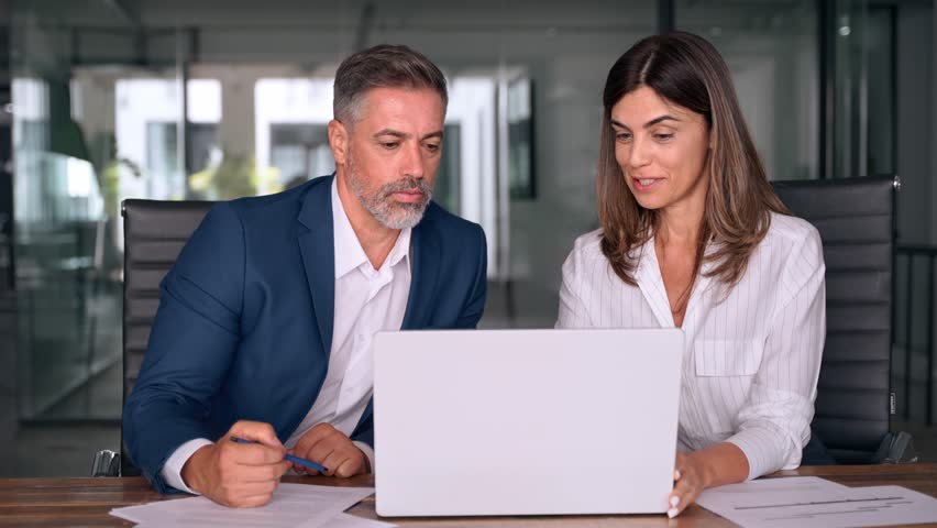 Team of diverse partners sitting at table mature Latin business man and European business woman discussing project on laptop in office. Two colleagues of professional business people working together. Royalty-Free Stock Footage #1107342075