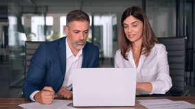 Team of diverse partners sitting at table mature Latin business man and European business woman discussing project on laptop in office. Two colleagues of professional business people working together. - Powered by Shutterstock - Get 15% off with code: PIKWIZARD15