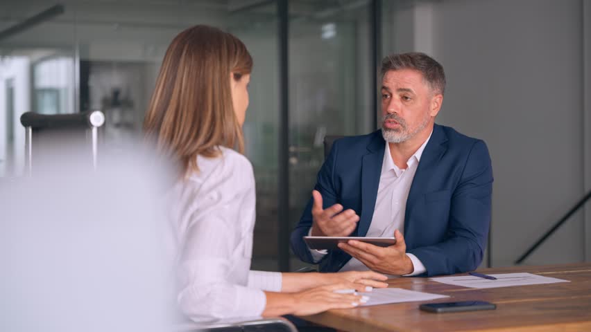 Team of diverse partners mature Latin business man and European business woman discussing project on tablet sitting at table in office. Two colleagues of professional business people working together. - Powered by Shutterstock - Get 15% off with code: PIKWIZARD15