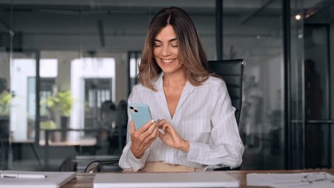 Smiling Latin Hispanic mature adult professional business woman using mobile phone cellphone. European businesswoman CEO holding smartphone using fintech application standing at workplace in office. 스톡 비디오