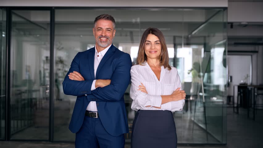 Portrait of smiling mature Latin or Indian business man and European business woman standing arms crossed in office. Two diverse colleagues, group team of confident professional business people. Royalty-Free Stock Footage #1107342099
