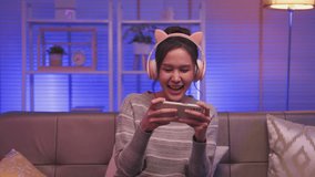 Happy asian woman gamer wear headphone participation play video game colorful neon n living room at night at  house.