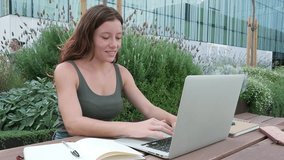 Redhead female university student doing homework using laptop and writing on notebook with pen. 4k resolution video.