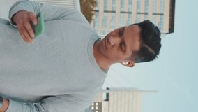 Vertical video, Athlete in wireless headphones, a guy in sportswear, walks along the bridge holding a mobile phone in his hands, listens to music