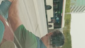 Vertical video, Middle-aged man dressed in casual clothes, waiting for tram at public transport stop in the city, view through the glass