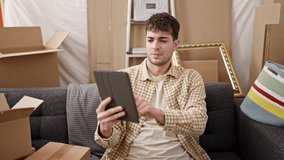 Young hispanic man doing video call sitting on the sofa at new home