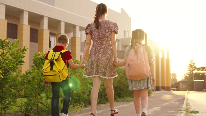 mother leads her son daughter by hand through school yard. children go to class holding mother hand. boy girl with mom. children backpacks backs go with mom lesson. kid holding mother hand. Royalty-Free Stock Footage #1107375567