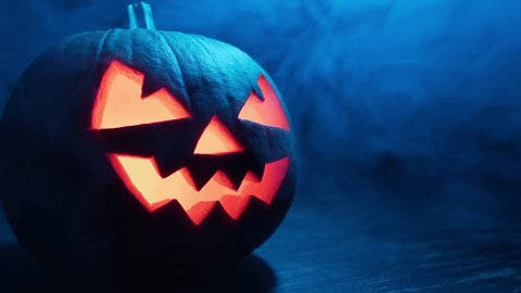Стоковое видео: Halloween pumpkin smile and scary eyes with smoke at dark background. Jack O' Lantern with blinking eyes. Halloween scary pumpkin. Spooky face glowing in dark. Close-up in 4K, UHD