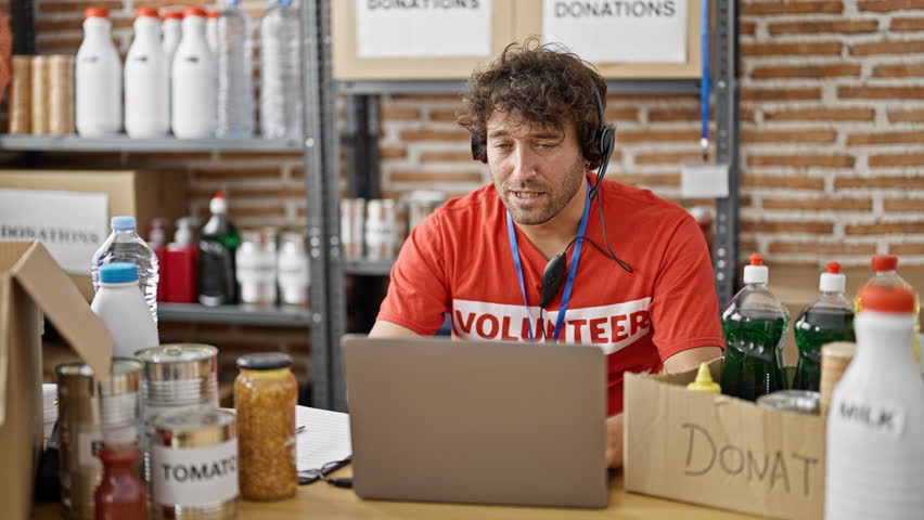 Young hispanic man volunteer writing on clipboard having video call at charity center