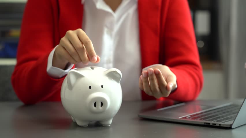 Woman sitting at desk managing expenses, calculating expenses, paying bills using laptop online, making household financial analysis, closer focus on the white piggy bank.  Royalty-Free Stock Footage #1107396249