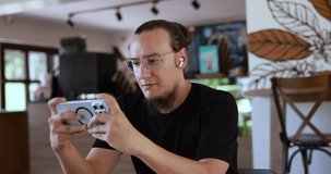 Young Man with Glasses Watching Video on Phone and Smiling While Wearing Headphones in Cafe 4K Slow Motion

SHOTLISTstrea