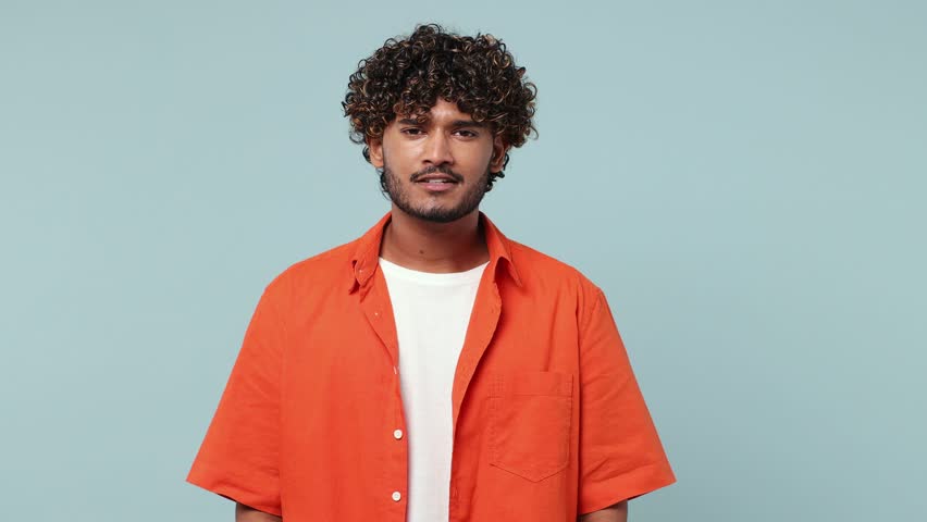 Excited jubilant overjoyed happy young Indian man wear red shirt casual clothes doing winner gesture celebrate clench fists say yes isolated on pastel plain light blue cyan background studio portrait