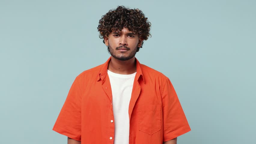 Joyful jubilant shocked young Indian man wear red shirt casual clothes say wow omg what spread hands doing winner gesture put arms on face screech isolated on pastel plain light blue cyan background