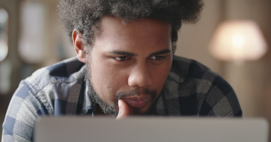 Young black man working on laptop. Male programmer working on code for new innovative stunning IT project. Black guy programmer immersed in work at laptop. Guy smiles, laughs, content with his project Royalty-Free Stock Footage #1107403453