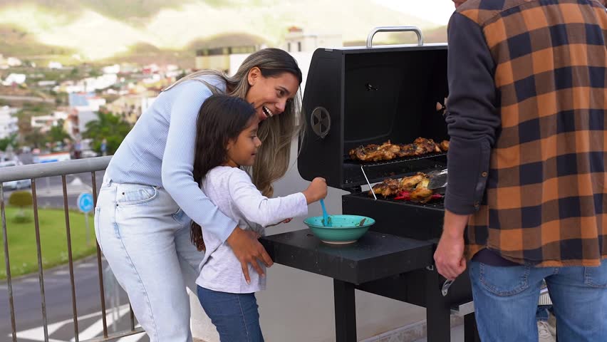 Happy latin female child marinating meat on barbecue grill - Multi generational people having fun doing bbq at house rooftop Royalty-Free Stock Footage #1107405475