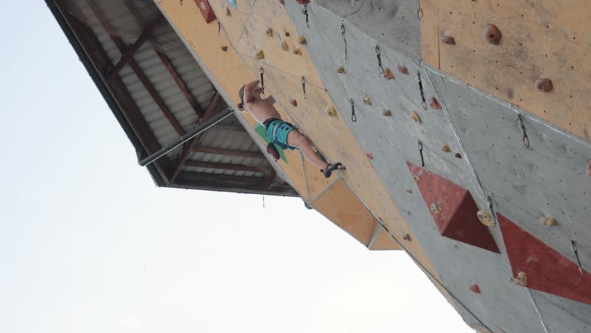 Athletic, strong, shirtless young man training outdoors, going down after climbing an artificial wall. Concept of extreme sport, hobby, active lifestyle, health and strength