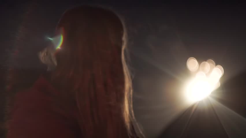 A girl, in a sweater, at night in a camping, on the beach of the sea, looks at a small bokeh fireworks in the sky. Chilly. Summer. Handheld shooting