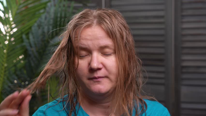 Portrait of tired woman with wet hair near palm tree, examines her hairstyle, sighs. Humid tropical climate Problem of damaged, dry hair Recovery, care Frustrated client touching curl with split ends | Shutterstock HD Video #1107417293
