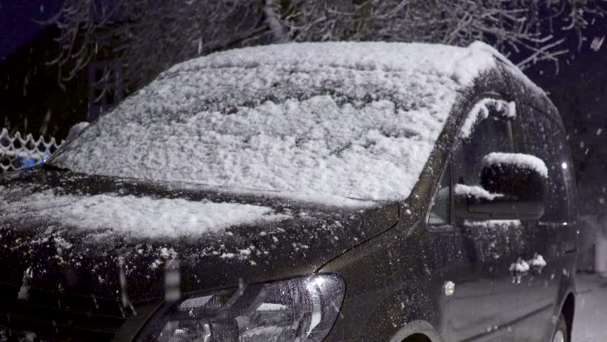 Snow falls on the car at night,in winter, there is a parked car and the snow is beautiful