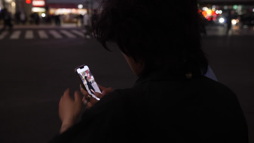 Girl checking images on her phone at night. Tokyo, Japan. 