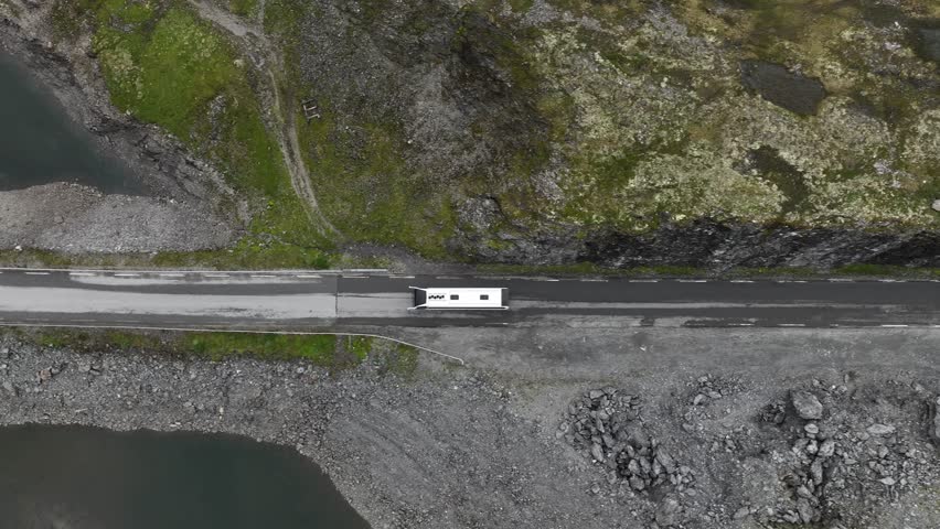 White bus crossing Vikafjellet mountain pass during summer - Top-down birdseye aerial following bus