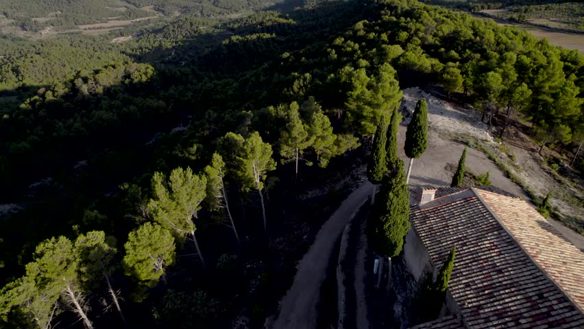 Backwards aerial revealing top view of an aisled Hermitage on top of a hill among trees in Spain