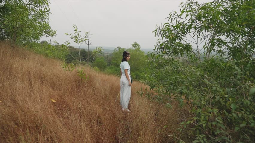 Cinematic shot of Girl tourist with umbrella at rural mountain in bushes. Girl poses for the camera as the camera move towards her. People at nature landscape. Young Girl exploring wild jungle. 