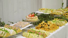 English buffet full of sandwiches and cakes on a long table inside a warehouse environment for a business meeting moving sideways revealing the foods and selection offered for the event