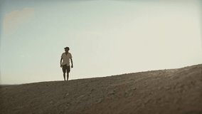 cinematic video of a man wearing summer clothes walking through the dessert on an extreemly hot day in the summetime.