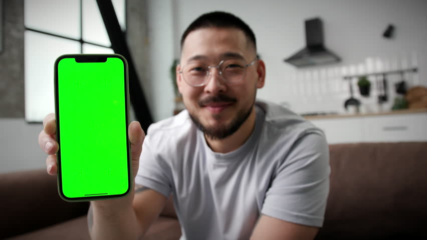 Smiling Asian Man Showing Mobile Phone Green Screen at Camera.