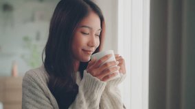 Attractive asian lady enjoying her morning coffee or tea at home, Smiling woman holding cup of tea in hands while looking out the window at morning. - Powered by Shutterstock - Get 15% off with code: PIKWIZARD15