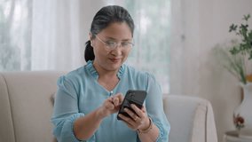 Strong elderly older grandmother feeling happy using mobile cell phone communicate with family enjoy retirement life in house.Happy Asian elderly woman smile and video call in living room at home.