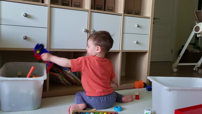 The child himself cleans up toys in the nursery after the game. Toddler baby collects toys in a box. Kid boy aged two years (two-year-old) Royalty-Free Stock Footage #1107440979