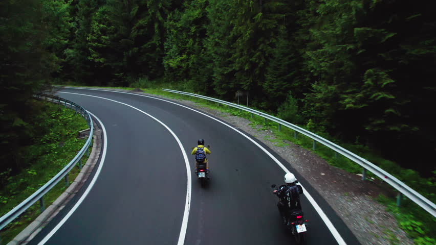 Aerial perspective of two friends riding motorbikes along mountain road surrounded by greenery